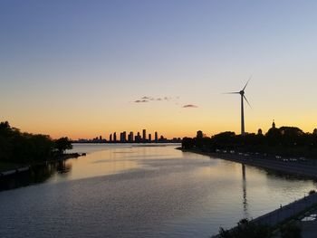 Silhouette traditional windmill by river against clear sky during sunset