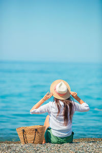 Rear view of woman in hat by sea against sky