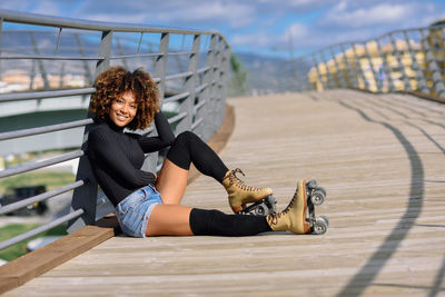 Portrait of mid adult woman with roller skates sitting on bridge