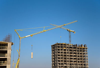 Low angle view of crane by building against clear blue sky