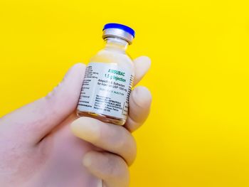 Close-up of hand holding bottle against yellow background