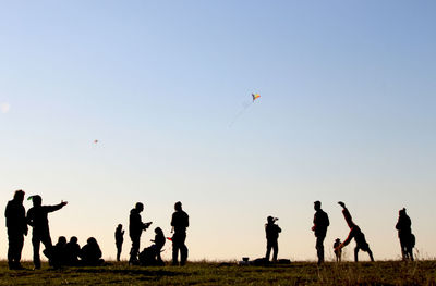 Silhouette people flying kite on field against clear sky during sunny day