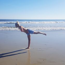 Side view of young woman exercising at beach against clear sky during sunny day