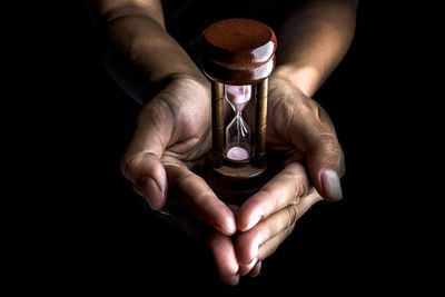 Cropped hands holding hourglass against black background