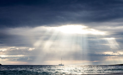 Idyllic shot of cloudy sky with sunbeam over sailboat in sea