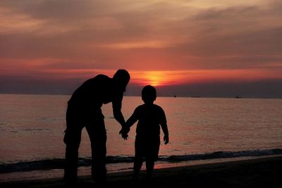 Silhouette boy standing on beach against sky during sunset