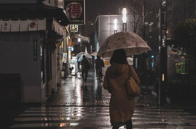 Rear view of woman walking on wet street at night