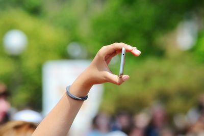 Cropped hand holding smart phone on sunny day