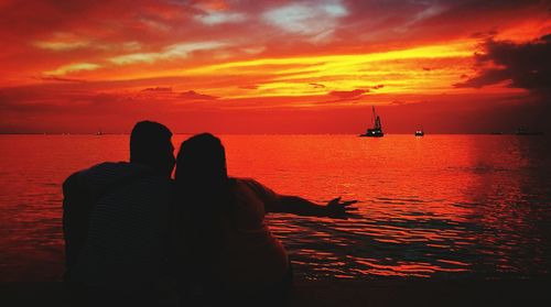 Silhouette men in sea against romantic sky at sunset