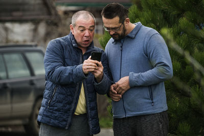 Full length of man holding smart phone while standing outdoors