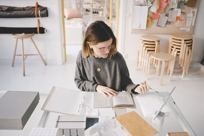 High angle view of female upholstery worker with documents sitting at desk in store