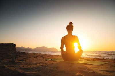 A woman meditates on the coast by the sea, rear view. yoga, health harmony, silhouette of a young