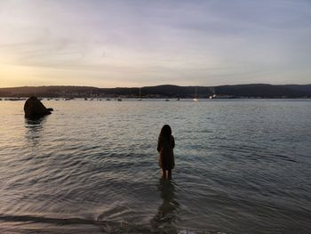 Rear view of woman standing in sea against sky