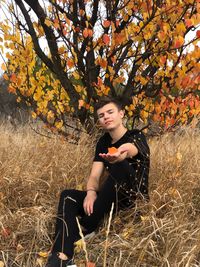 Young woman looking away while sitting on tree during autumn