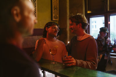 Young gay couple talking to each other while standing at bar counter