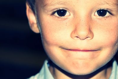 Close-up portrait of cute smiling boy against black background