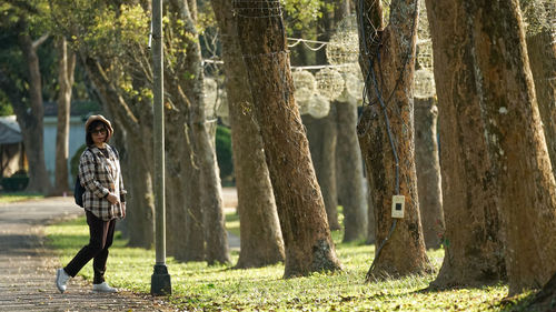 Portrait of woman standing by tree trunk in forest