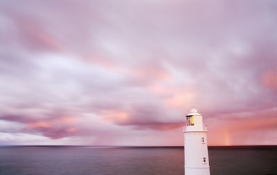 Lighthouse by sea against sky during sunset