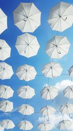 Low angle view of umbrellas hanging against blue sky