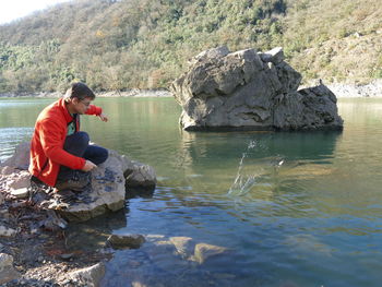 Side view of man sitting by lake on rock