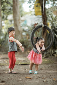 Full length of baby girl by brother holding tire swing