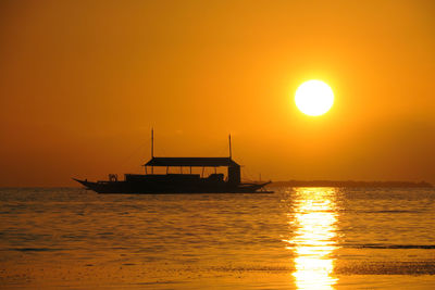 Silhouette ship in sea against orange sky