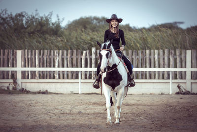 Portrait of woman sitting on horse in ranch against sky