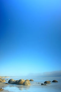Rocks in sea against clear blue sky
