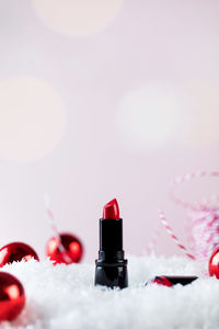 Red lipstick tube and christmas tree baubles on artificial snow pile