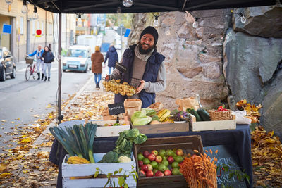 Portrait of happy man standing with vegetable basket at market stall