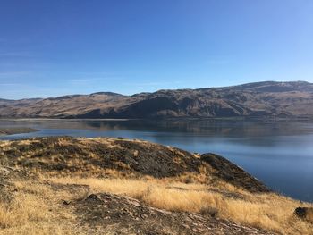 Scenic view of lake and mountains against clear blue sky