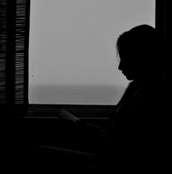 Side view of silhouette woman reading books in house