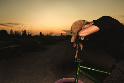 Side view of man holding umbrella on road against sky during sunset