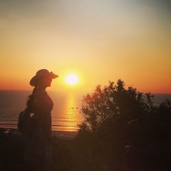 Silhouette person standing by sea against sky during sunset