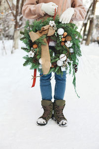 Low section of woman holding christmas decoration standing on snow