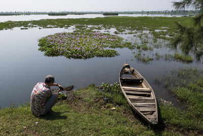 Man photographing boat moored on lakeshore during sunny day