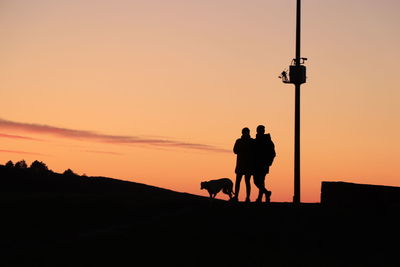 Silhouette people standing on street against sky during sunset