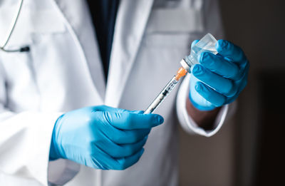 Doctor in white coat drawing vaccine into a syringe for injection.
