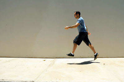 Side view of man levitating over sidewalk by wall