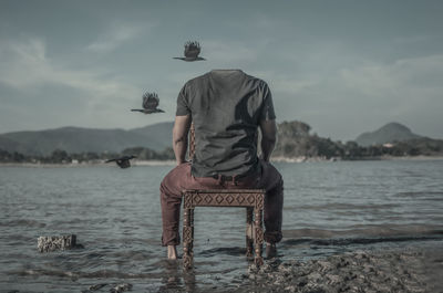 Rear view of man standing in sea against sky