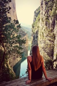Rear view of woman looking at view sitting on wooden seat against rock formation