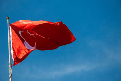 Low angle view of red flag against blue sky