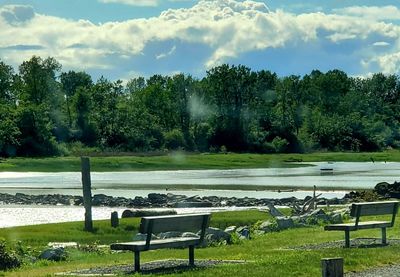 Empty bench by lake against sky