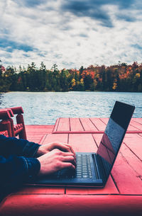 A freelance male taking outdoors in autumn, laptop by the lake. blurred bkgrd - aged effect filtered