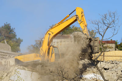 Yellow crawler excavator demolishes dilapidated real estate for future construction of modern house