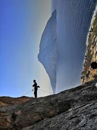 Silhouette man rope climbing mountain against sea and mountain