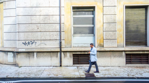 Full length of man walking on footpath against building