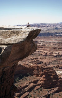 Woman sitting on mountain against sky during sunny day at canyonlands national park