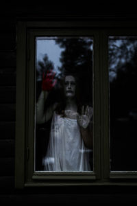 Female ghost with blood on hand seen through glass window of haunted cabin