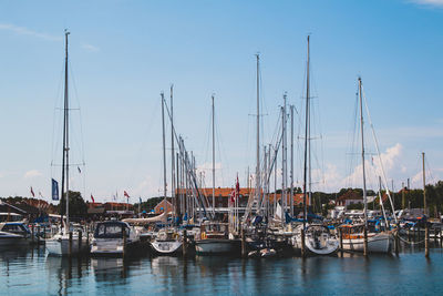 Sailboats moored at harbor against blue sky
